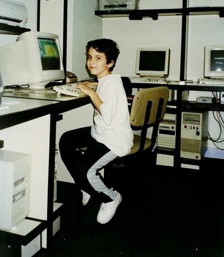 Felipe Drummond criança, sentado diante de um computador num laboratório de informática.